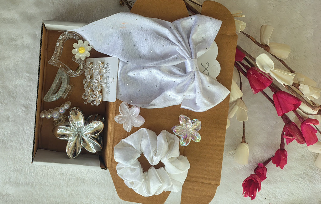 Set of hair accessories including scrunchies and clips in a box on a textured surface with flowers.