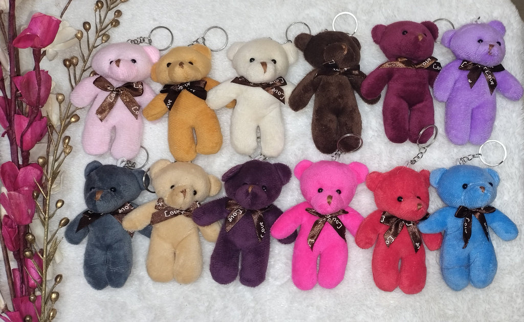 Colorful teddy bear keychains arranged on a white towel with a wooden surface and pink flowers in the background.